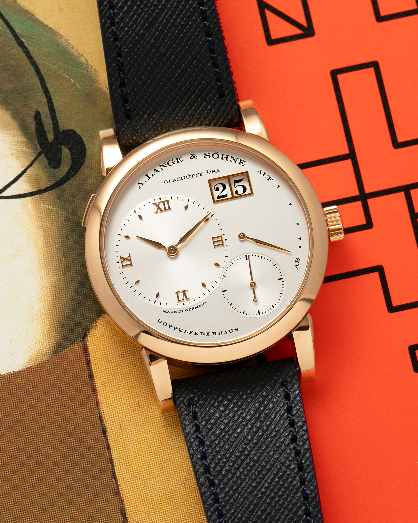Brand: A. Lange & Sohne Year: 2000s Model: Lange 1 Reference: 101.032 Material: 18-carat Rose Gold, German Silver Movement: A. Lange & Söhne Cal. L901.0, Manual-Winding Case Diameter: 38.5mm Lug Width: 20mm Strap: Molequin Navy Blue Textured Calf Leather Strap with Signed 18-carat Rose Gold Tang Buckle, with additional A. Lange & Söhne Black Alligator Leather Strap (Used)