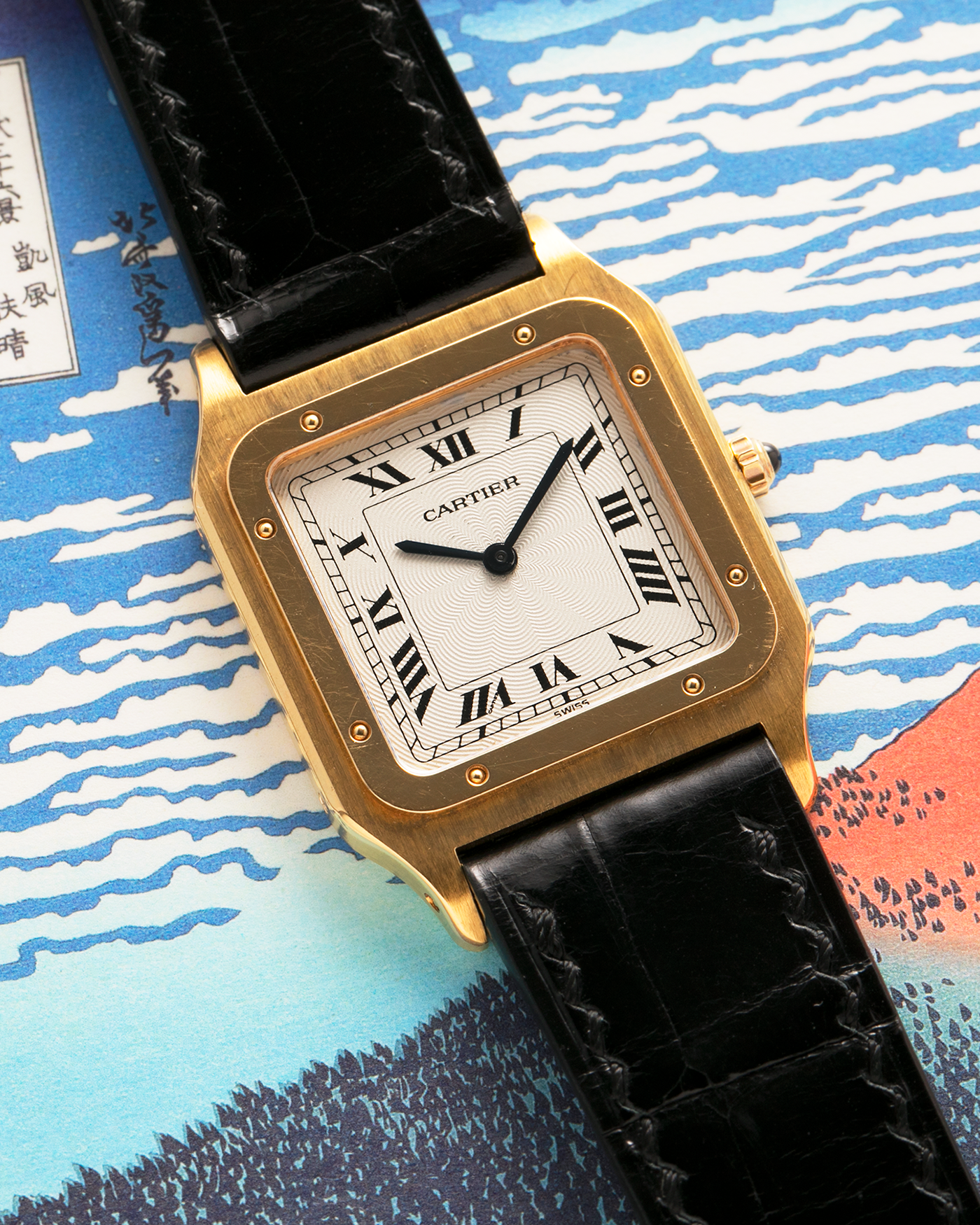 Brand: Cartier
Year: 1990s
Model: Santos Dumont
Reference: 1576
Material: 18-carat Yellow Gold
Movement: Cartier Cal. 021MC (Based on Frédéric Piguet 21 ébauche), Manual-Winding
Case Dimensions: 27mm x 6.5mm (Lug-to-Lug 36mm)
Lug Width: 17mm
Strap: Generic Unnamed Black Calf Leather Strap with Cartier Style Gold Plated Tang Buckle, Cartier Black Alligator Leather Strap