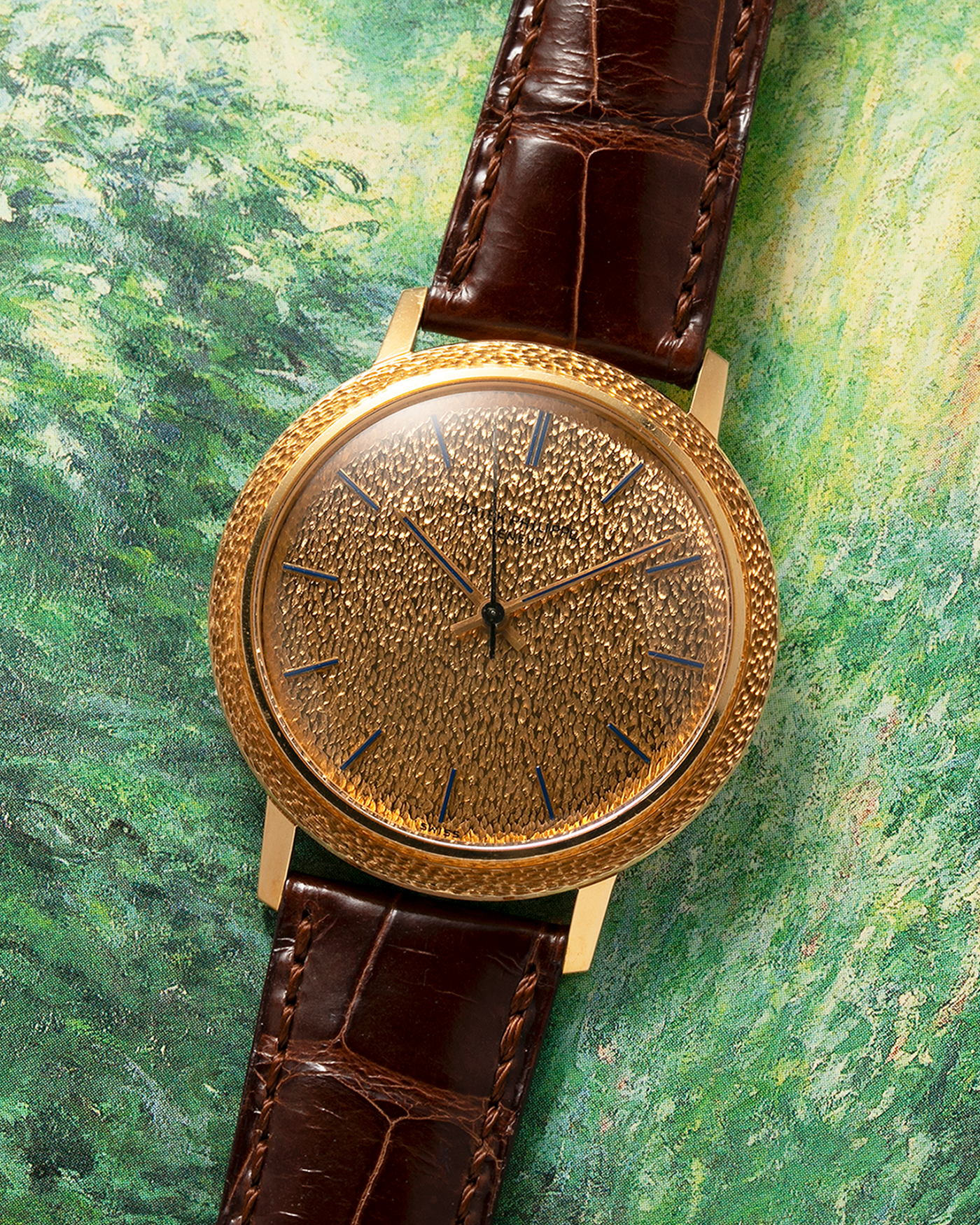 Brand: Patek Philippe
Year: 1970
Model: Calatrava ‘Back Wind’ Hammered
Reference Number: 3569J
Material: 18-carat Yellow Gold
Movement: Patek Philippe Back-Wind Cal. 350, Self-Winding
Case Dimensions: 36mm x 8.3mm (Lug-to-Lug 41mm)
Lug Width: 18mm
Strap: Patek Philippe Dark Brown Alligator Leather Strap with Signed 18-carat Yellow Gold Tang Buckle