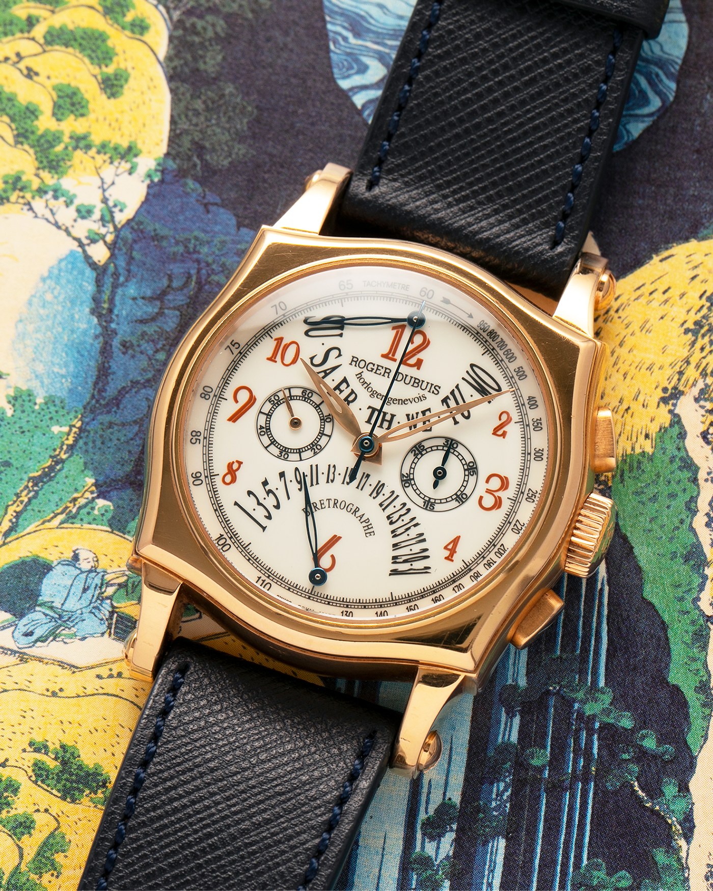 Brand: Roger Dubuis
Year: 2000s
Model: Sympathie 40 Biretrograde Chronograph
Material: 18-carat Yellow Gold
Movement: Roger Dubuis Cal. RD 5630 (Based on the Lemania Cal. 2310), Manual-Winding
Case Dimensions: 40mm x 12.25mm (Lug-to-Lug 47mm)
Lug Width: 22mm
Strap: Molequin Navy Blue Textured Calf Leather Strap with Signed 18-carat Yellow Gold Tang Buckle