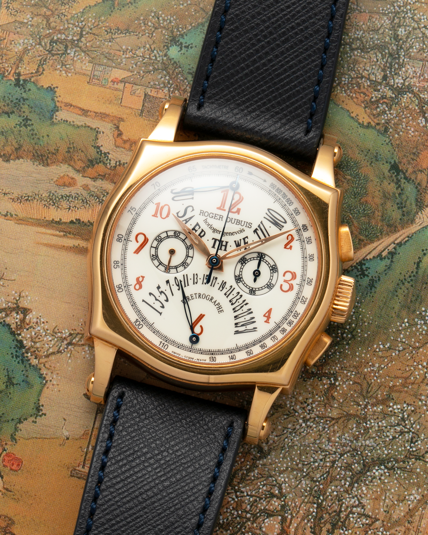 Brand: Roger Dubuis
Year: 2000s
Model: Sympathie 40 Biretrograde Chronograph
Material: 18-carat Yellow Gold
Movement: Roger Dubuis Cal. RD 5630 (Based on the Lemania Cal. 2310), Manual-Winding
Case Dimensions: 40mm x 12.25mm (Lug-to-Lug 47mm)
Lug Width: 22mm
Strap: Molequin Navy Blue Textured Calf Leather Strap with Signed 18-carat Yellow Gold Tang Buckle