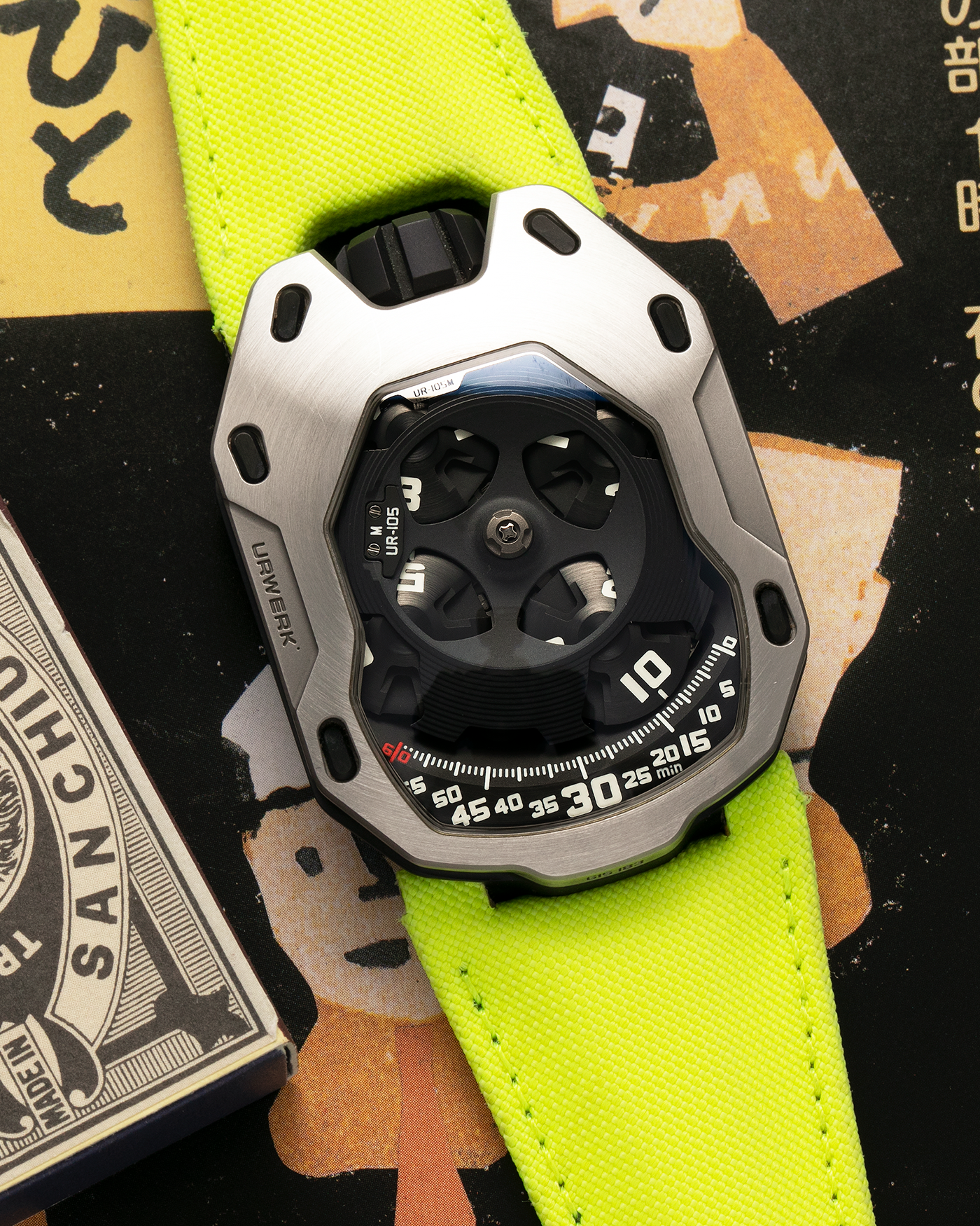 Brand: Urwerk Year: 2014 Model: UR105M “Iron Knight”, Limited to 77 pieces Material: Stainless Steel, Titanium Movement: Urwerk Cal. 5.01, Manual-Winding Case Dimensions: 39.50mm x 53mm x 16.65mm Strap: Urwerk Fluorescent Yellow Textile Strap with Signed Titanium Tang Buckle