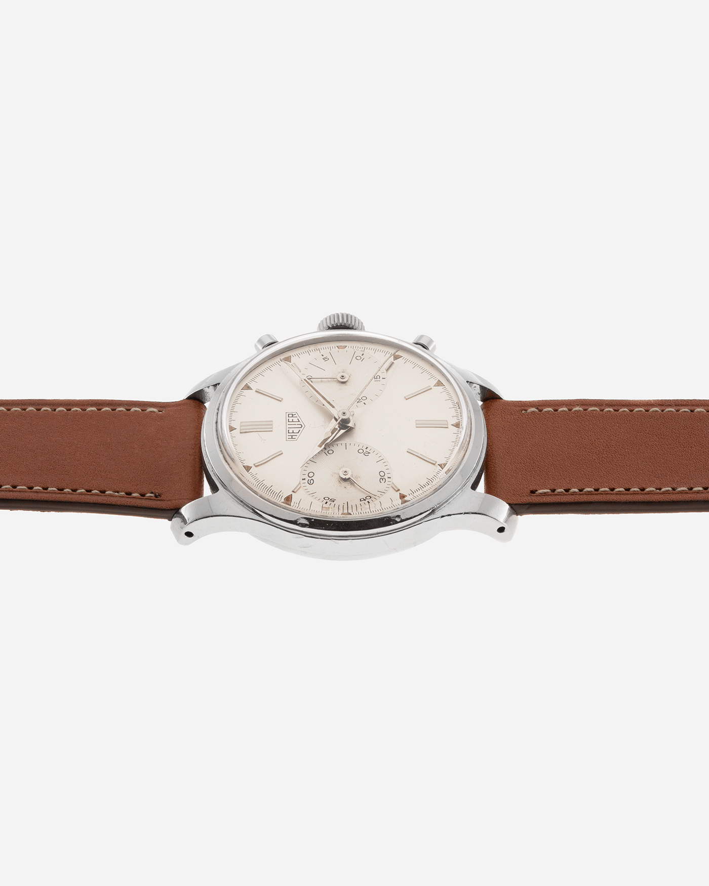 Brand: Heuer Year: 1950’s Reference Number: 404 Material: Stainless Steel Movement: Valjoux 23 Case Diameter: 34mm Lug Width: 18mm Bracelet/Strap: Nostime Gold Tan Barenia Smooth Calf