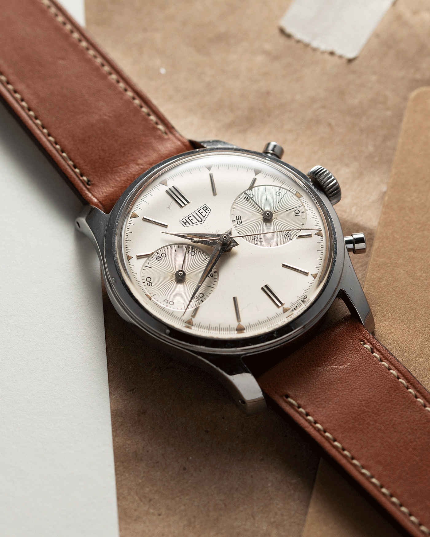 Brand: Heuer Year: 1950’s Reference Number: 404 Material: Stainless Steel Movement: Valjoux 23 Case Diameter: 34mm Lug Width: 18mm Bracelet/Strap: Nostime Gold Tan Barenia Smooth Calf