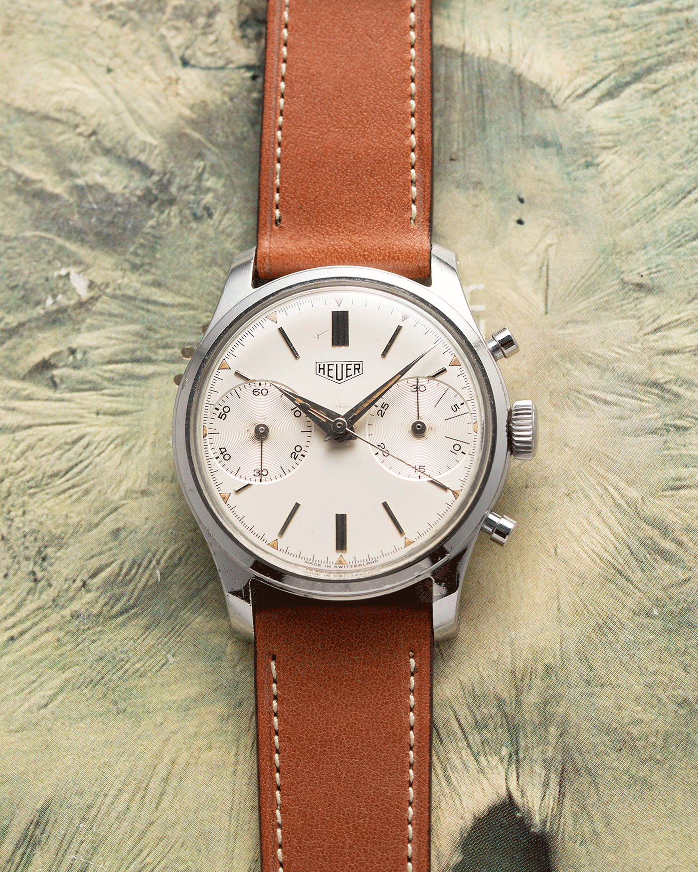 Brand: Heuer Year: 1950’s Reference Number: 404 Material: Stainless Steel Movement: Valjoux 23 Case Diameter: 34mm Lug Width: 18mm Bracelet/Strap: Nostime Gold Tan Barenia Smooth Calf